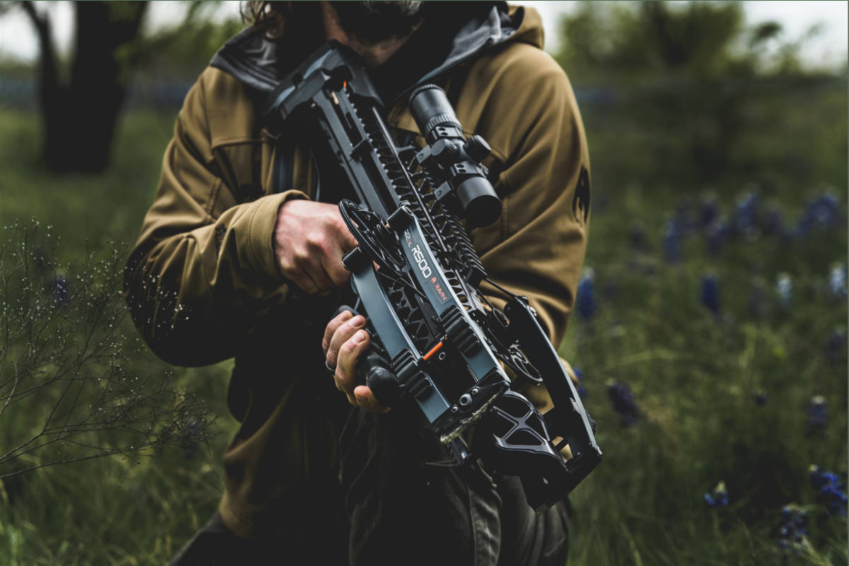 #takticar_u_smedjoj_jakni_drzi_crni_ravin_crossbows_r500_samostrel_sa_pricvrscenim_nisanom_na_travnatom_polju_prva_linija#