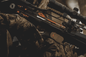 krupni plan crno-narandžastog ravin crossbows lovacki samostreli sa montiranim nisanom, koji drzi osoba u kamuflaznim lovackim rukavicama u mracnom, otvorenom okruzenju prva linija 1